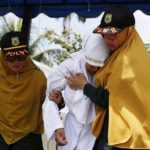 Terrified Indonesian woman is escorted by police before being caned in public for having sex outside marriage in violation of Sharia law